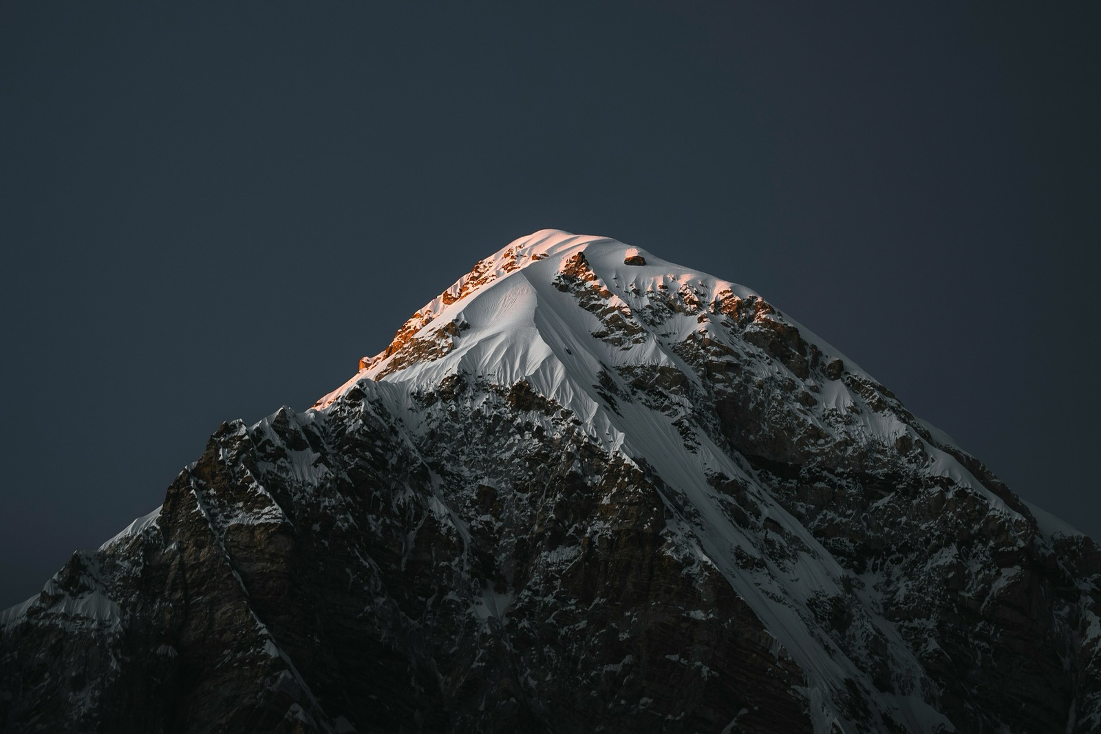 A snow-capped mountain summit catching the last warm light of sunset against a darkening sky
